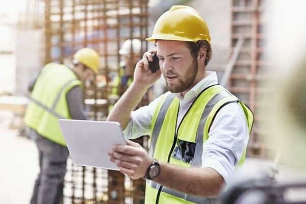 engineer with digital tablet talking on cell phone VqJ0NJ - How Can SMS Reporting Benefit Your Construction Site?