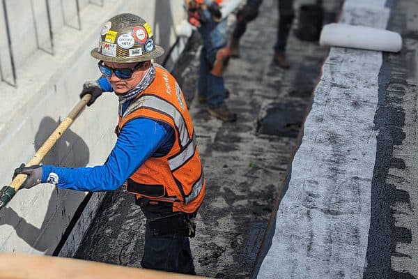 Man waterproofing concrete wall