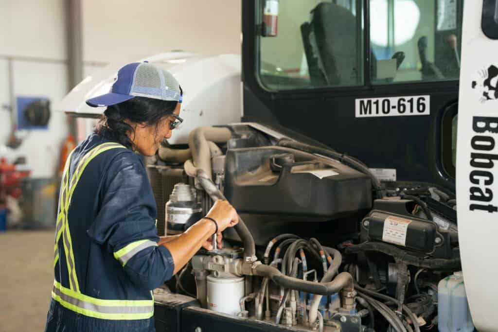 Woman in construction gear works on a truck.