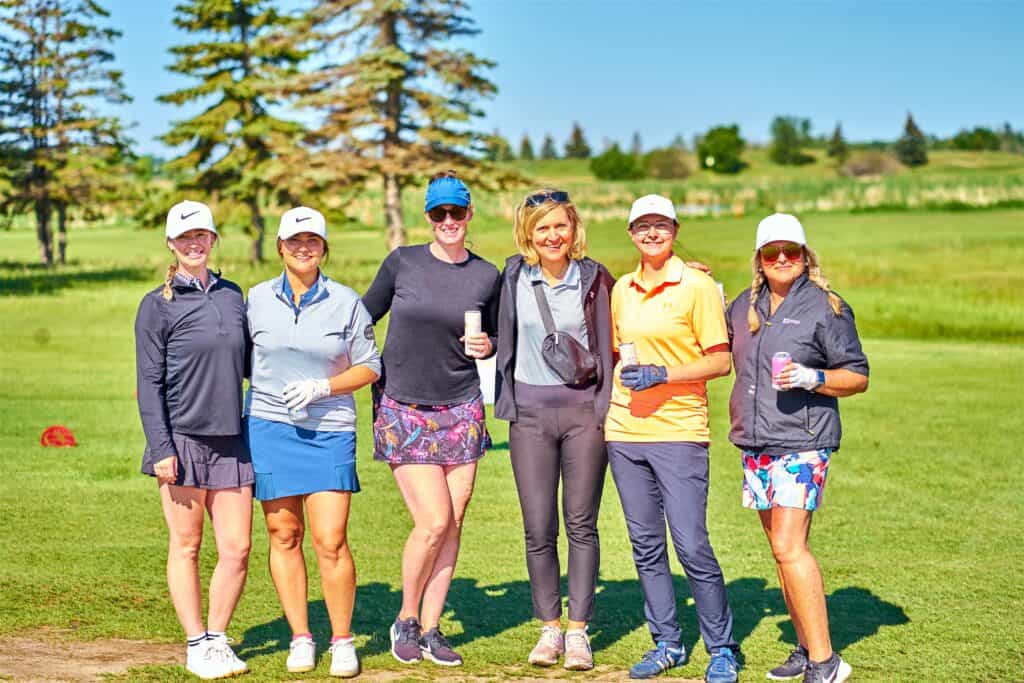 A group of women in sports clothing stand on a golf course smiling.